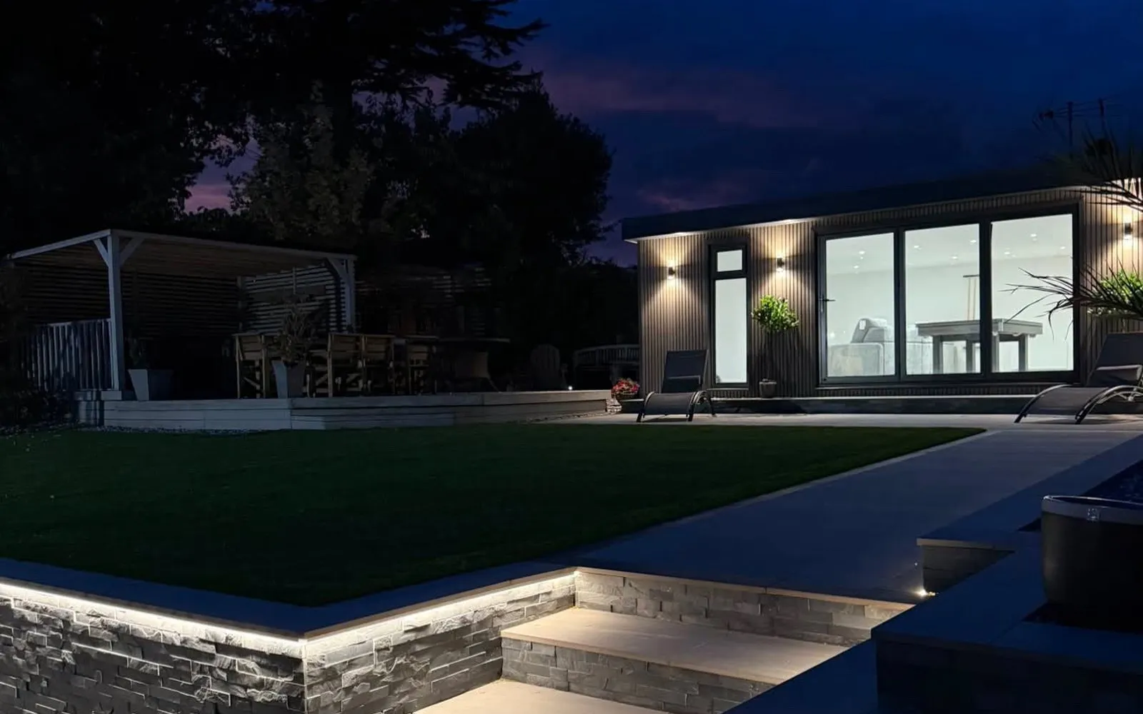 LED-lit stone steps leading up to a bespoke garden entertainment room at night
